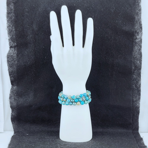 Three Chrysocolla bracelets stacked on a white mannequin hand display against a dark textured background.