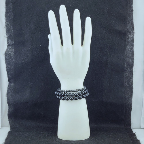 Two Shungite bracelets stacked on a white mannequin hand display against a dark textured background.