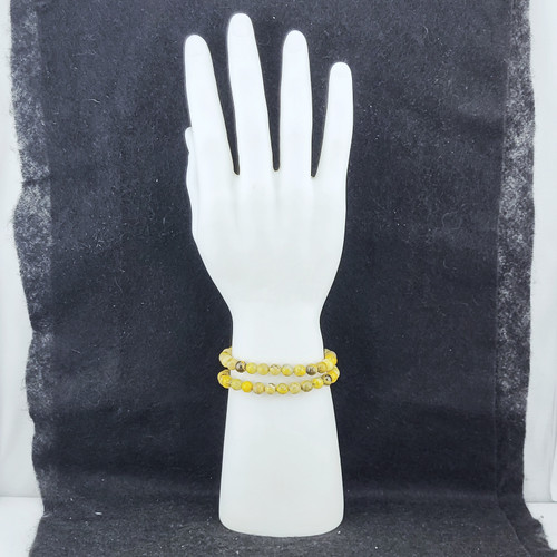 A stack of Bumblebee Jasper bracelets displayed on a white mannequin hand against a dark background.