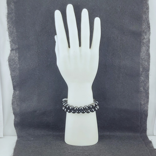 A stack of Gold Sheen Obsidian bracelets displayed on a white mannequin hand against a dark background.