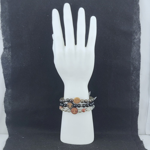 Three stone bracelets with wooden Tree of Life charms stacked on a white display hand against a black background.