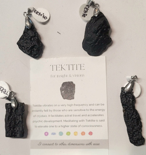 Four unique raw black Tektite pendants with silver bails arranged around an informational card.