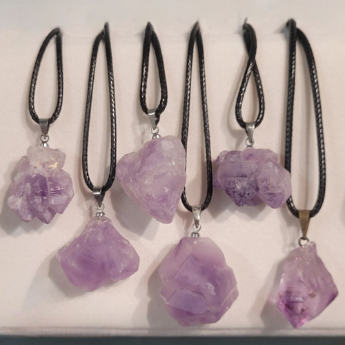 A collection of six unique raw Amethyst crystal pendants on black cords showcasing various natural light purple formations.