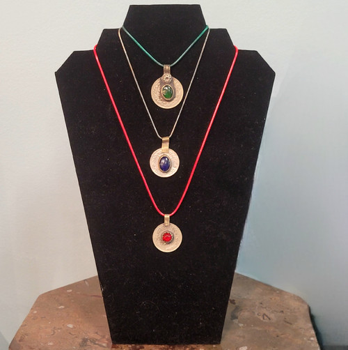 Three vintage-style coin necklaces with green, blue, and red gemstones displayed on a black velvet jewelry bust.
