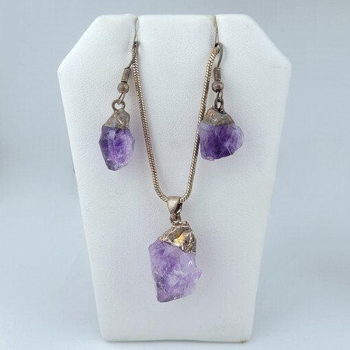 Raw Amethyst crystal jewelry set featuring a pendant on a silver snake chain and matching drop earrings on a white display stand.