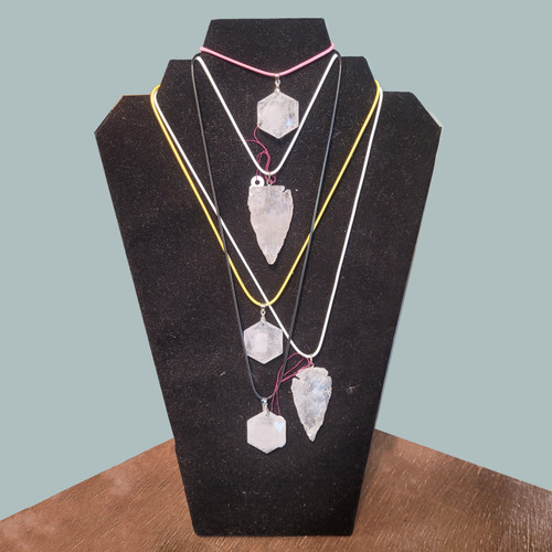 A collection of Clear Quartz necklaces in arrowhead and hexagon shapes on pink, black, and white cords displayed on a jewelry bust.