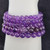 A detailed close-up shot of several deep purple polished Amethyst beads showing natural translucency and white mannequin arm.