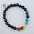 A Black Onyx stretch bracelet featuring seven colorful chakra gemstone beads and silver accent spacers on a white background