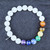 A Selenite stretch bracelet featuring white beads and seven colorful chakra gemstone beads on a clean white background.