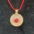 Close-up of a circular bronze-tone coin pendant with a faceted red stone on a bright red cord.