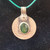 Detail of an antiqued silver-style coin pendant featuring an oval green gemstone cabochon on a green cord.