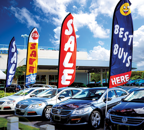 Swooper flags on poles shown flying over cars in a dealership lot