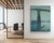 An oversized vertical fine art print of James Whistler’s Nocturne: Blue and Gold – Old Battersea Bridge, styled in a modern residential living room. The large, moody indigo and teal print hangs unframed on a light wall behind a white boucle accent chair and two round wood side tables.