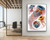 A large-format vertical print of Ernst Haeckel’s Discomedusae jellyfish illustration displayed on a plain white wall in a corporate office. To the left of the print, a floor-to-ceiling glass partition shows a modern conference room with a light wood table, black office chairs, and an exposed wood beam ceiling.