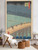 An oversized vertical print of Hiroshige’s Japanese woodblock print, Sudden Shower over Shin-Ohashi Bridge, styled in a modern residential living room. The large artwork hangs on a light grey wall directly behind a white boucle accent chair and two round, natural wood side tables on a light area rug.