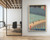 A large-format vertical print of Hiroshige’s Sudden Shower over Shin-Ohashi Bridge displayed on a white wall in a commercial office setting. To the left of the print, a floor-to-ceiling glass partition shows a modern conference room with a light wood table, black office chairs, and exposed wood ceiling beams.