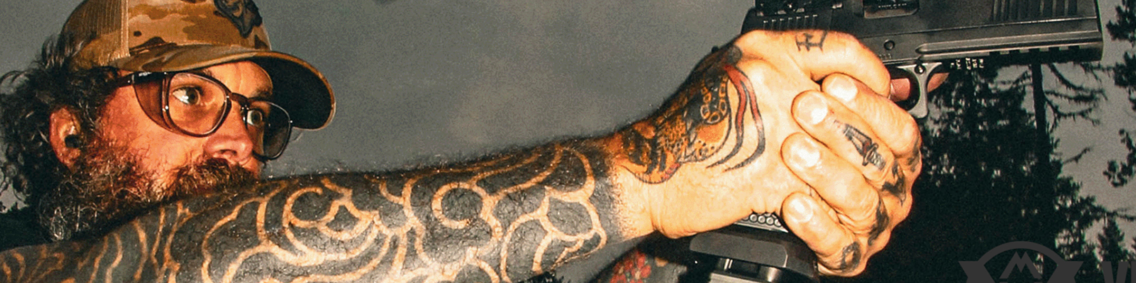 Person holding a handgun showing detailed arm tattoos